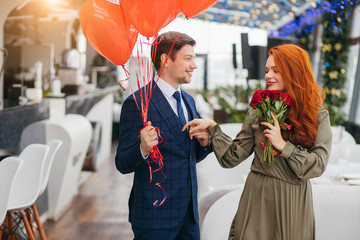 caucasian elegant man and attractive redhaired lady in dress on a date in restaurant, gallant...