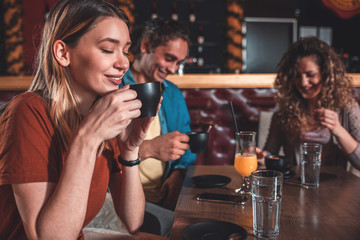 Portrait of young woman enjoying drinking coffee in cafe with her friends.