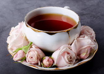 Tea time backdrop with vintage white porcelain tea cup, gentle pink roses on a dark gray background.