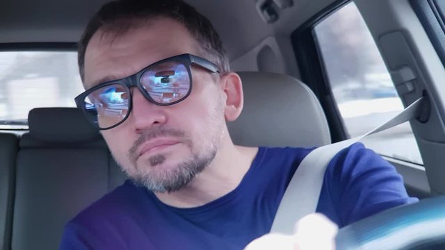 Caucasian man drives passenger car and makes turn. Very strong reflection in his glasses