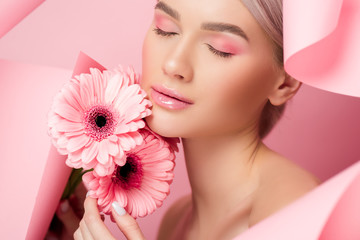 tender girl with closed eyes holding pink flowers in torn paper, on pink