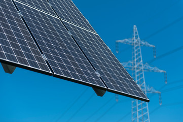 Photovoltaik Anlage Nahaufnahme mit unscharfem Hochspannungsmast dahinter, blauer Himmel, Nahaufnahme mit unscharfem Detail im Hintergrund, Querformat