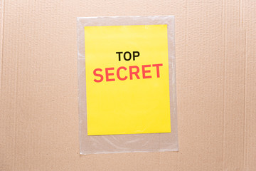 Secret writes on yellow paper and transparent plastic bag with cardboard box background. Business access, privacy and confidential concept.