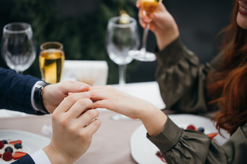 putting golden ring on a woman's finger. romantic caucasian guy makes marriage proposal to beautiful redhaired lady in dress, woman agree to marry. indoors. love, marriage, couple, romantic date