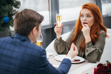 love, celebration, anniversary concept. marriage proposal to beautiful woman by young man. handsome guy in elegant tuxedo sit with attractive redhaired lady in restaurant. couple in love