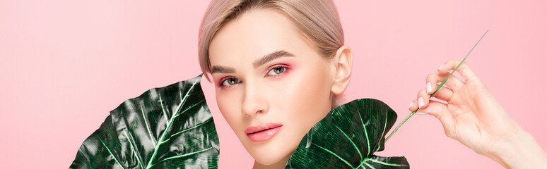 panoramic shot of attractive girl with pink makeup isolated on pink with green leaves