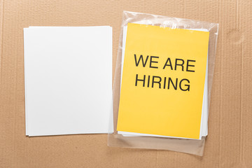 Curriculum vitae concept with yellow banner "we are hiring" on beige cardboad box background. Job search concept.