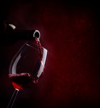 Red wine pouring in wineglass from bottle over dark background.