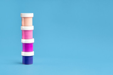 Colorful vibrant cans of gouache paint isolated on color blue background. Painting background. A set of acrylic paints in jars for the artist. Copy space. The concept of creativity and minimalism