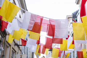 Dutch square flags on a ribbon, in red, white and yellow, of traditional festival named Carnaval, like Mardi Gras, in 's-Hertogenbosch, Oeteldonk with a blue sky