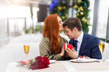 young handsome generous guy in tuxedo congratulates his redhaired girlfriend with saint valentines day or birthday. woman thanks man, kiss him on the forehead. emotions, love, celebration concept