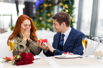 couple celebrate birthday of redhaired woman in restaurant. beautiful lady in dress experiencing vivid emotions with her boyfriend in tux, handsome guy is real gentleman. love, romantic, celebration