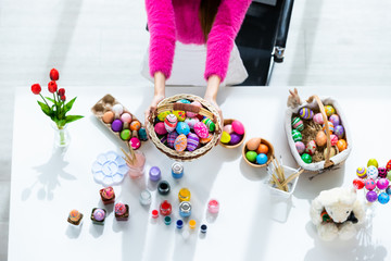 Easter holiday concept,Close up of Happy Asian Young woman hand holding a basket with colorful Easter eggs on white wooden table background in top view