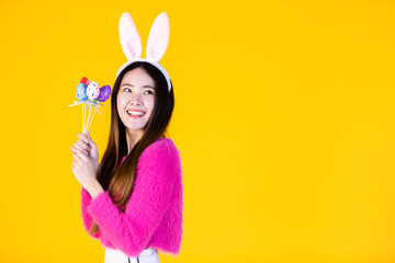 Easter holiday concept, Happy smile Asian Young woman hand holding colorful Easter eggs Skewers In isolated on Yellow blank copy space studio background.