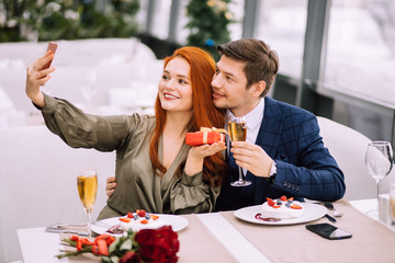 beautiful caucasian lady take selfie with handsome man in restaurant, couple on a date. young man and woman have romantic evening, they celebrate anniversary or birthday, wearing party clothes