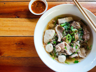 Close-up of Thai Noodle Soup with Meat in white bowl and dipping sauce on wooden background.