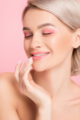 happy tender girl with pink makeup touching lips, isolated on pink