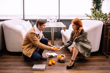 gallant caucasian man in jacket squatted down, help woman to collect tangerines from the floor....