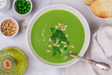 Homemade delicacy green pea soup cream with mint and pine nuts in a white plate on a marble table. Summer vegetable vegetarian (vegan) dish. Healthy diet. Selective focus, top view