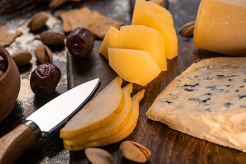 close up view of cheese platter with knife, sliced pear, pistachios, olives and crackers