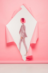 stylish woman in suit and pink wig posing in torn paper, on white