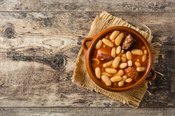 Typical Spanish fabada asturiana in crockpot on wooden table. Top view. Copy space