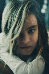 sad looking girl behind rain covered window. composite.