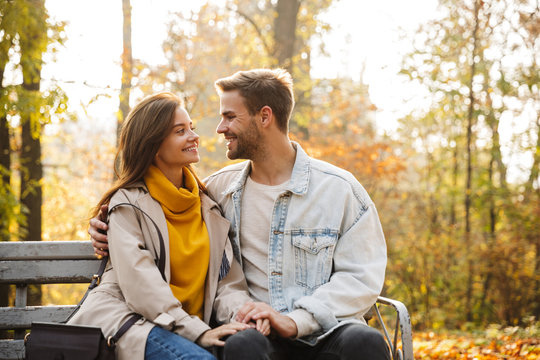 Image of attractive caucasian couple sitting on bench in autumn park