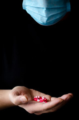 A man in a blue protective medical mask holds multi-colored tablets in his hand. Virus