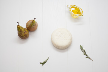 Round white cheese, sour milk, decorated with rosemary and olive oil, two ripe pears. The concept of types of cheese or dairy products rich in calcium.