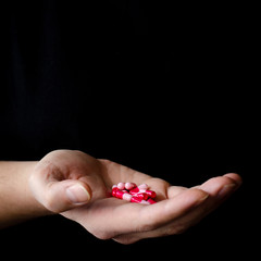 A man's hand in a black T-shirt holds multicolored antiviral tablets.