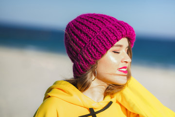 Young beautiful woman in yellow sweatshirt and bright purple knit hat on the beach
