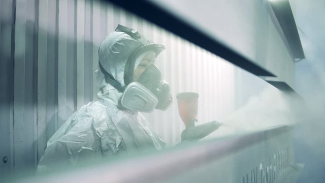 A woman in safety wear is spraying paint on metal