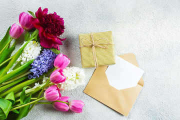 Obraz na płótnie Canvas Mother's day or Woman's Day Concept. Hyacinth, tulips and pion flowers, empty card and gift present on ligth concrete background. Spring Greeting card. Flat lay, top view, copy space. Mockup concept.