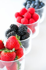 Assortment of fresh berries on a white background. Raspberries, blueberries, blackberries, strawberries in small glasses. Healthy eating. Vegan food. 