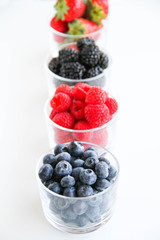 Assortment of fresh berries on a white background. Raspberries, blueberries, blackberries, strawberries in small glasses. Healthy eating. Vegan food. 