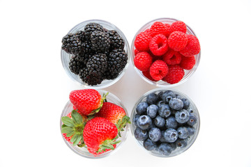 Assortment of fresh berries on a white background. Raspberries, blueberries, blackberries, strawberries in small glasses. Healthy eating. Vegan food. 