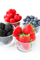 Assortment of fresh berries on a white background. Raspberries, blueberries, blackberries, strawberries in small glasses. Healthy eating. Vegan food. 