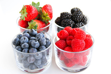 Assortment of fresh berries on a white background. Raspberries, blueberries, blackberries, strawberries in small glasses. Healthy eating. Vegan food. 