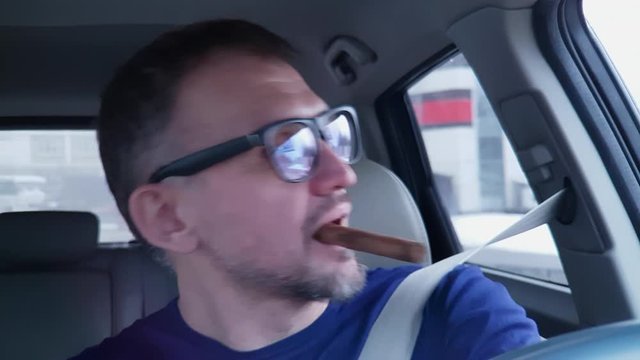 White man with beard driving moving car, smiling, taking cigar in his mouth, making a turn