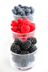 Assortment of fresh berries on a white background. Raspberries, blueberries, blackberries, strawberries in small glasses. Healthy eating. Vegan food. 
