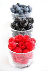Assortment of fresh berries on a white background. Raspberries, blueberries, blackberries, strawberries in small glasses. Healthy eating. Vegan food. 