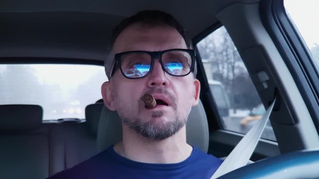 White bearded man behind steering wheel of passenger car takes unlit cigar in mouth