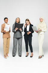 Obraz premium attractive multicultural businesswomen with folders near woman talking on smartphone on white