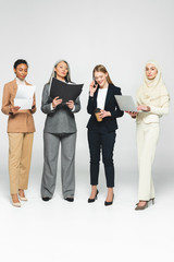 Obraz premium multicultural businesswomen with folders near woman talking on smartphone on white