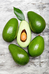 Fresh ripe organic green avocados and halve with leaf on gray concrete background, top view food concept. Minimal flat lay style avocados on gray concrete background