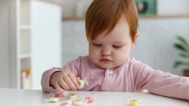 cute little baby girl fiddling with candies on the table at home
