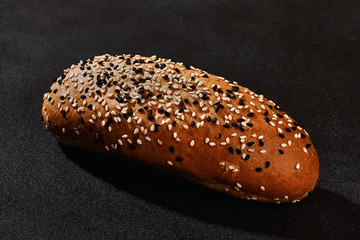 Fresh, palatable baked bread sprinkled with black and white sesame seeds against black background with copy space. Rural cuisine or bakery. Close-up