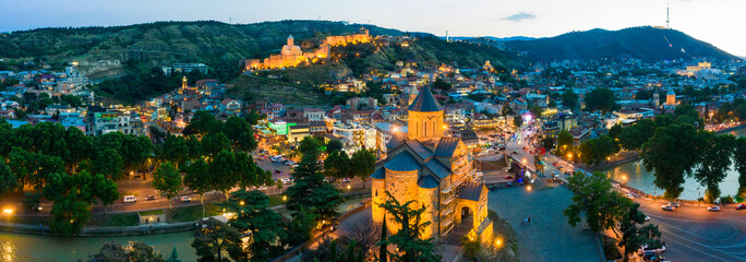 The evening panorama of the old town in the old district of Avlabari, Virgin Mary Metekhi church and Rike Park, the Kura river reflects the evening city lights in Tbilisi, Georgia. © miklyxa