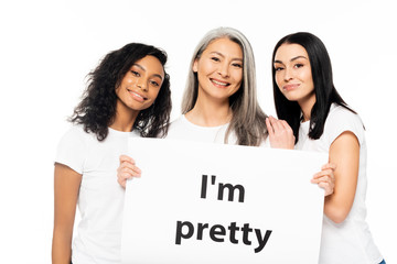 happy multicultural women near i`m pretty placard isolated on white